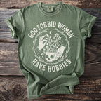 Green t-shirt with "GOD FORBID WOMEN HAVE HOBBIES" text and skull plant graphic.