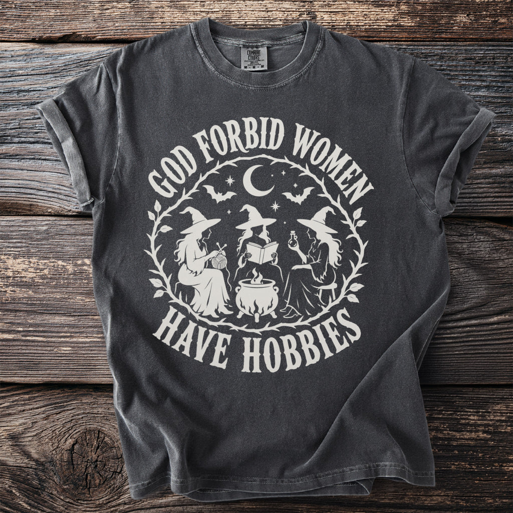 Dark grey t-shirt with "God forbid women have hobbies" text and witch illustration.