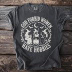 Dark grey t-shirt with "God forbid women have hobbies" text and witch illustration.