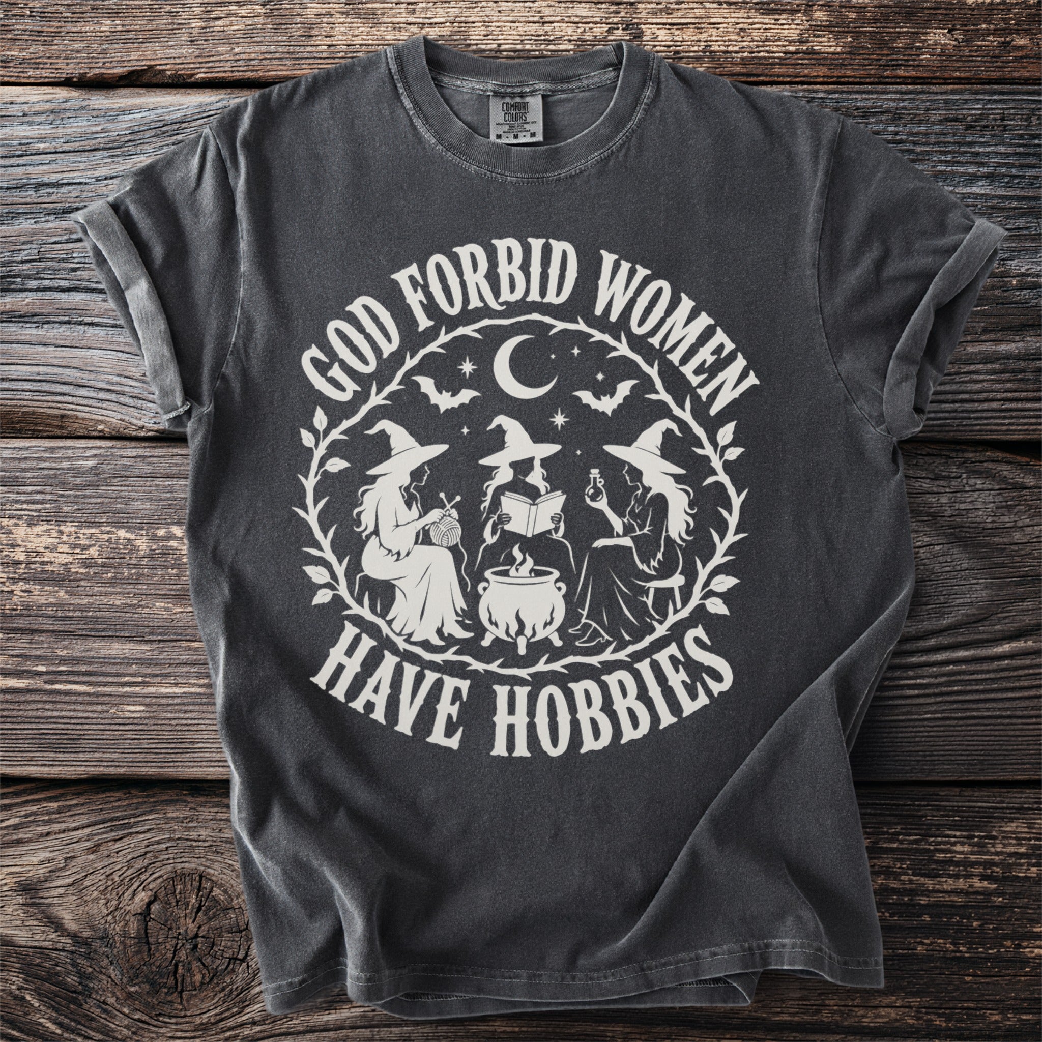 Dark grey t-shirt with "God forbid women have hobbies" text and witch illustration.