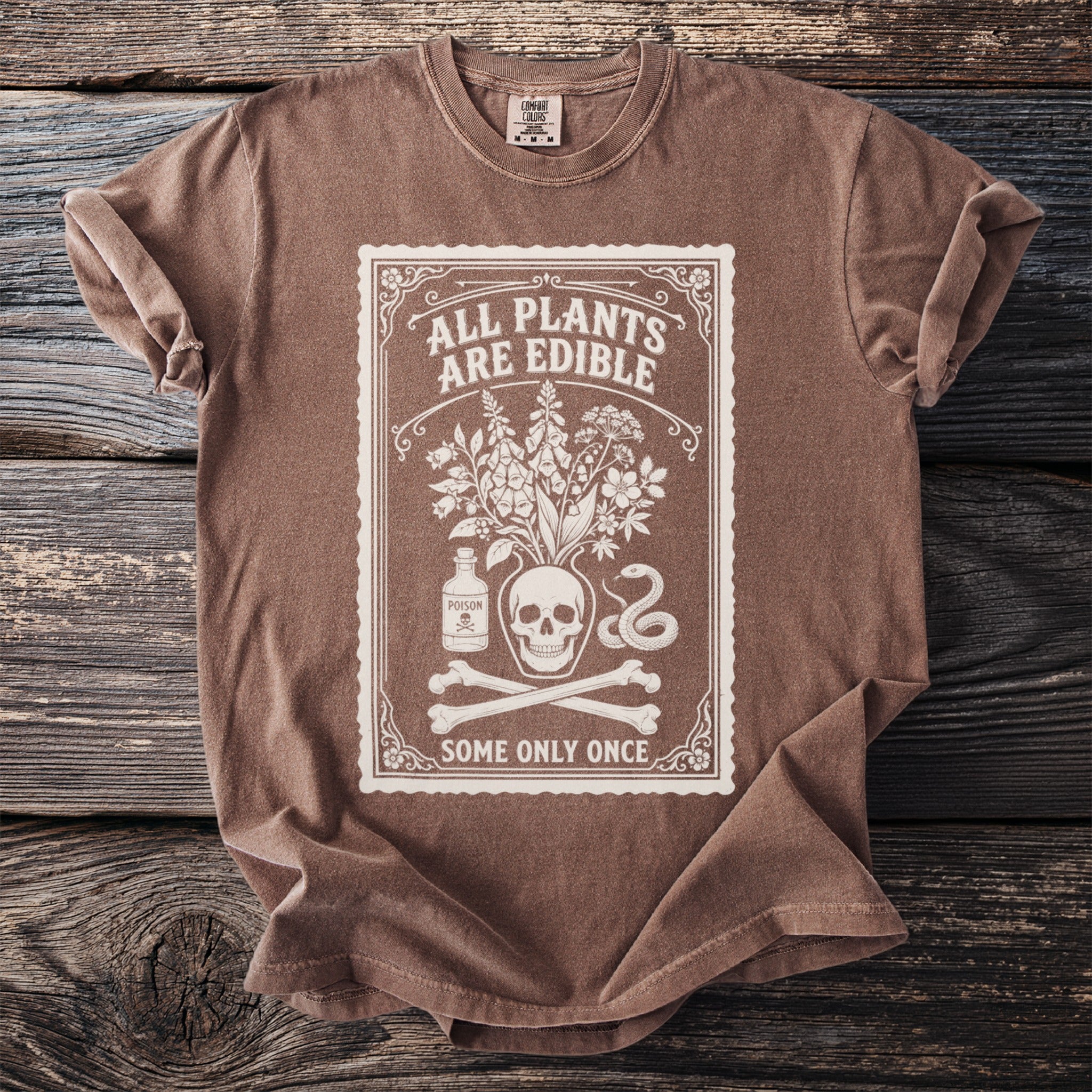 Brown t-shirt with white graphic of skull, plants, poison bottle, snake, and bones.