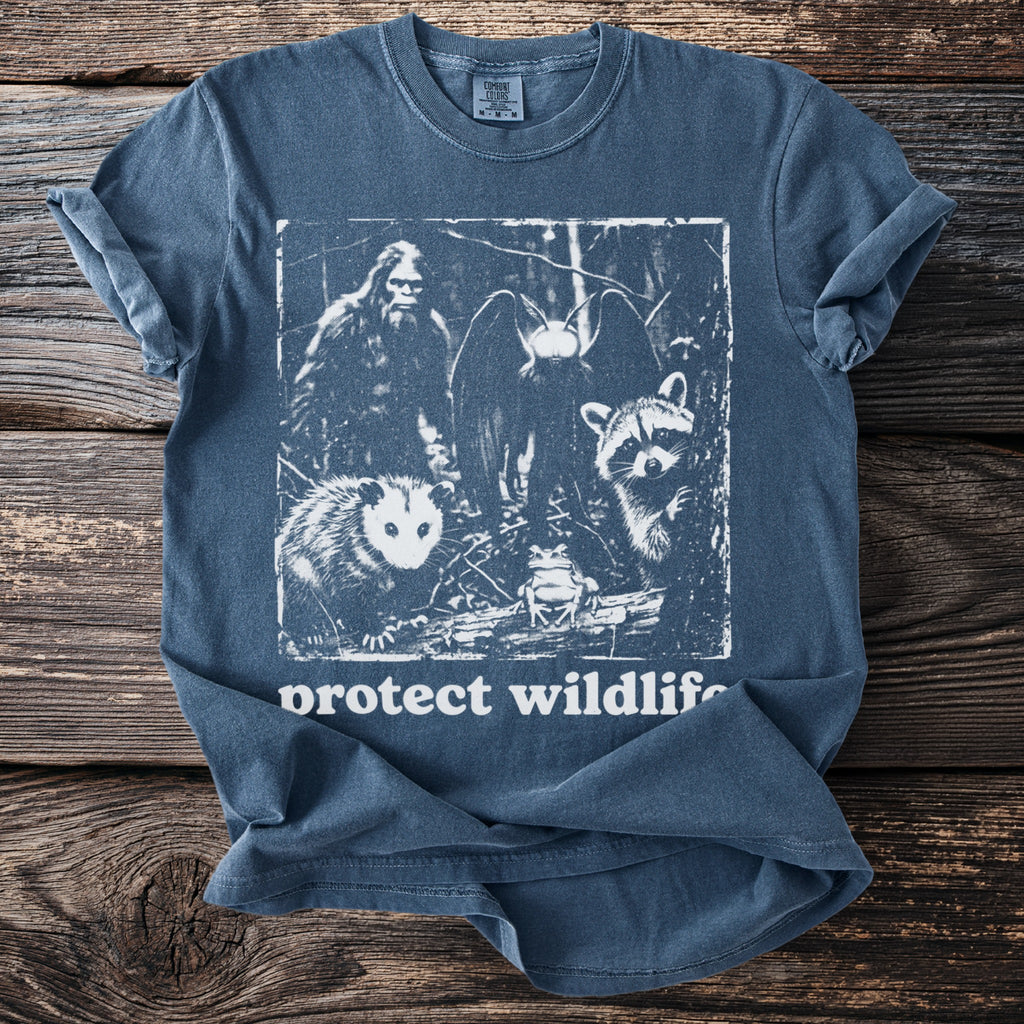 Blue t-shirt graphic features Bigfoot, moth, raccoon, opossum, and frog with "protect wildlife" text.