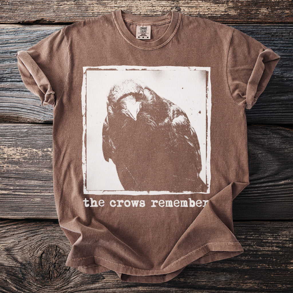Brown t-shirt with a white graphic of a crow's head and text "the crows remember".
