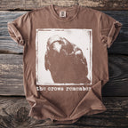 Brown t-shirt with a white graphic of a crow's head and text "the crows remember".