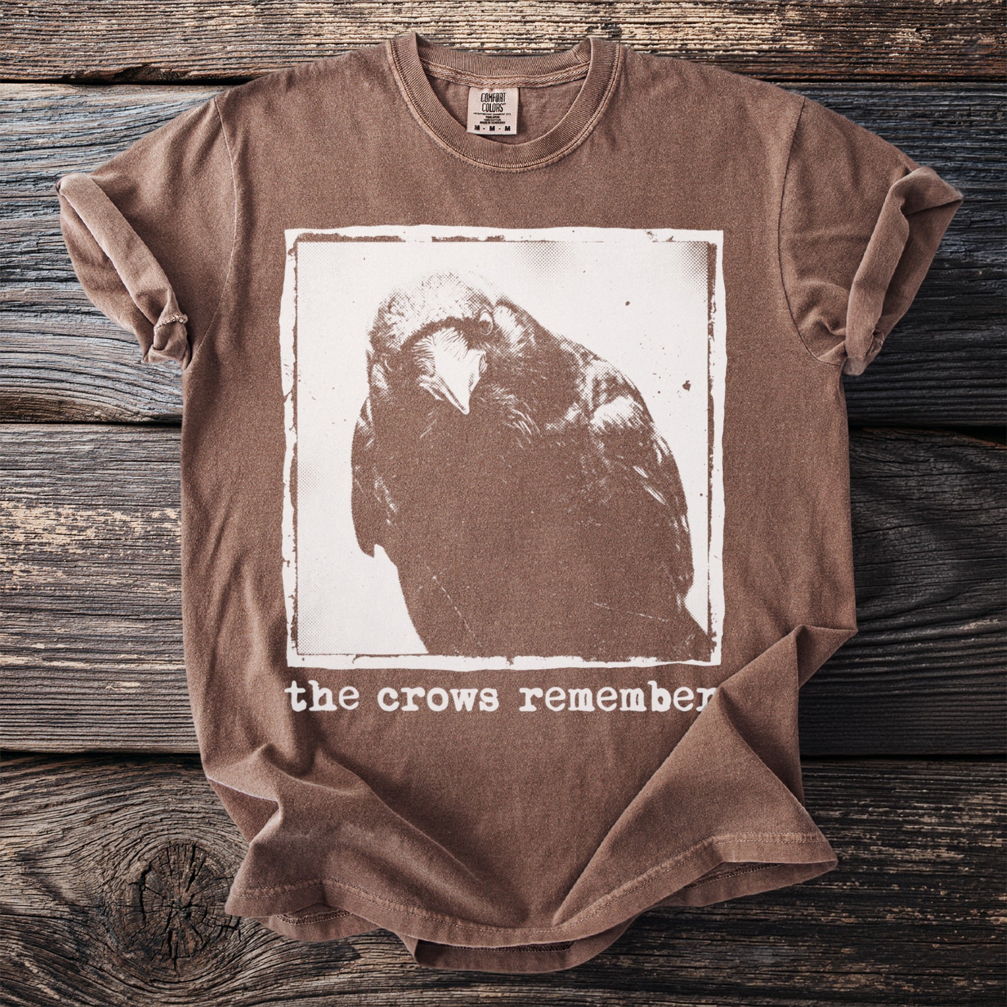 Brown t-shirt with a white graphic of a crow's head and text "the crows remember".