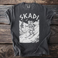 Dark grey t-shirt with "SKADI" text and a sketched scene of a skier on a mountain.