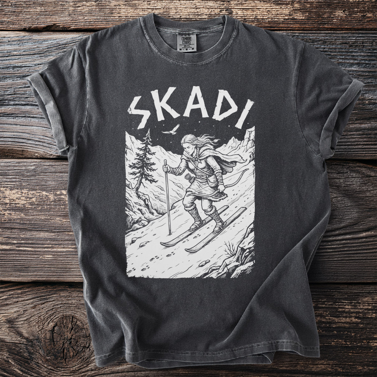 Dark grey t-shirt with "SKADI" text and a sketched scene of a skier on a mountain.