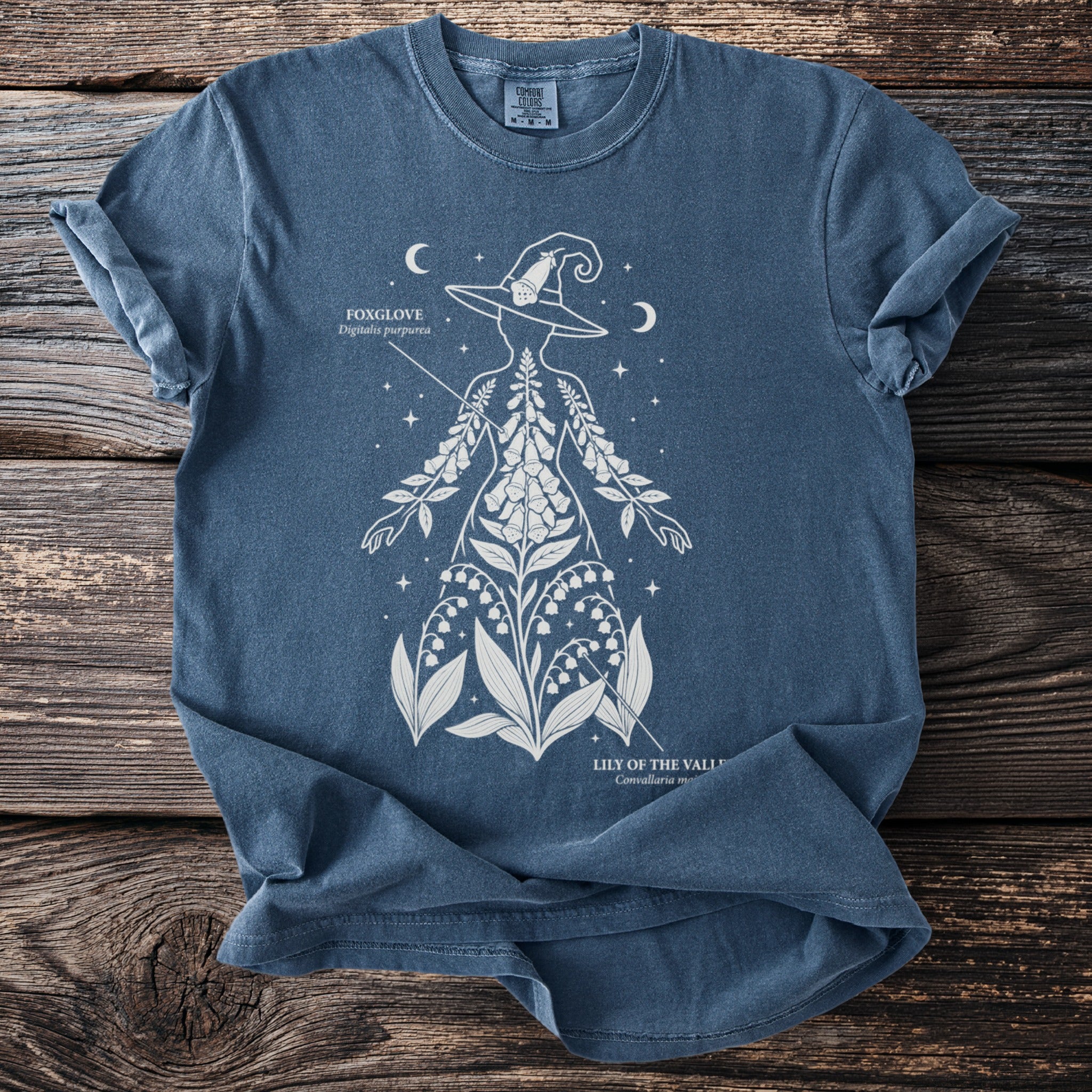 Blue t-shirt featuring a white outline of a person with foxglove and lily of the valley plants.
