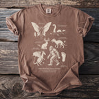 T-shirt with a "The Cryptid Field Guide" design featuring outlines of Mothman, Loch Ness Monster, Chupacabra, Jackalope, Jersey Devil, and Sasquatch.