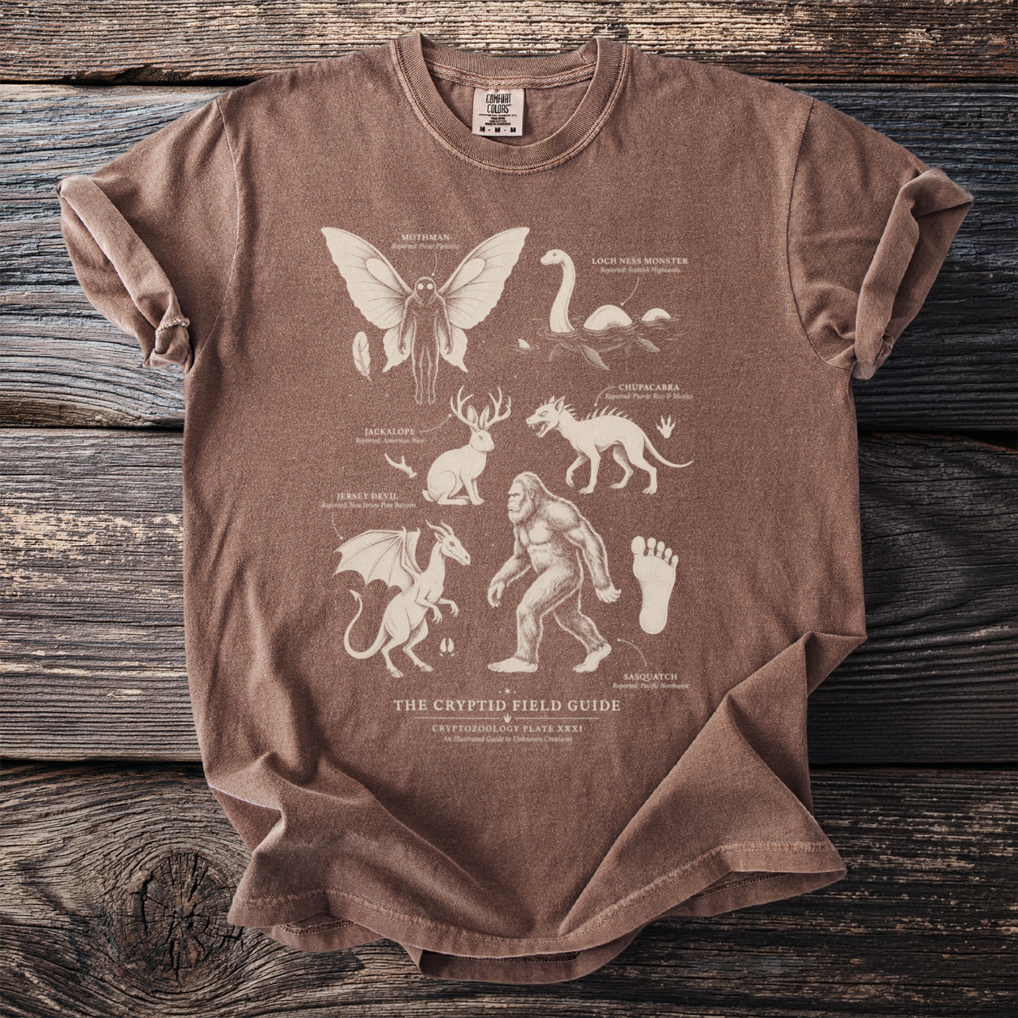 T-shirt with a "The Cryptid Field Guide" design featuring outlines of Mothman, Loch Ness Monster, Chupacabra, Jackalope, Jersey Devil, and Sasquatch.