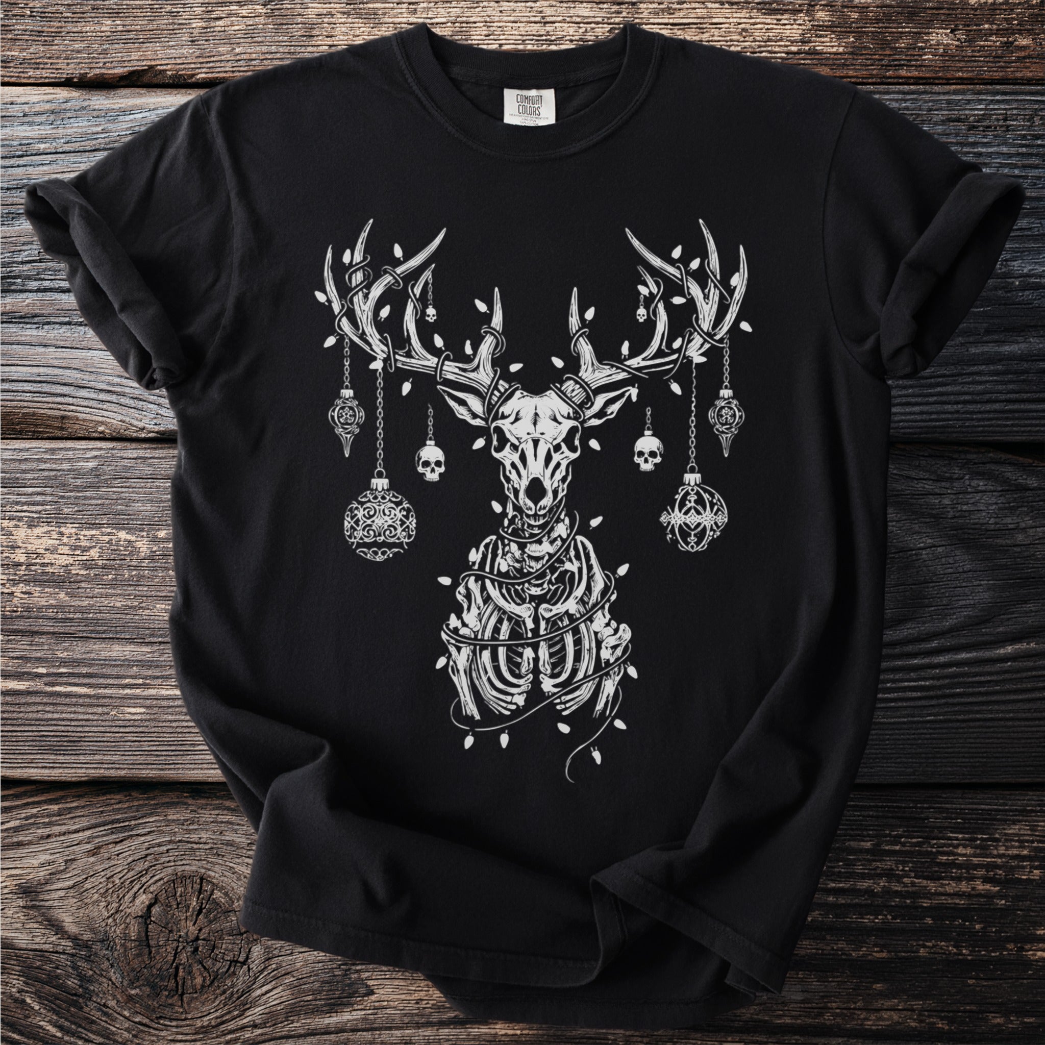 Black t-shirt with skeletal deer, skulls, and ornaments on wooden background.