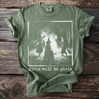 Green t-shirt with three figures in witch hats around a bonfire, text reads "girls will be girls".
