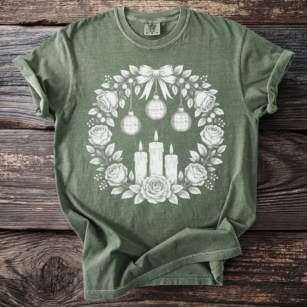 Green t-shirt with a white floral wreath, candles, and ornaments graphic.