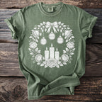 Green t-shirt with a white floral wreath, candles, and ornaments graphic.
