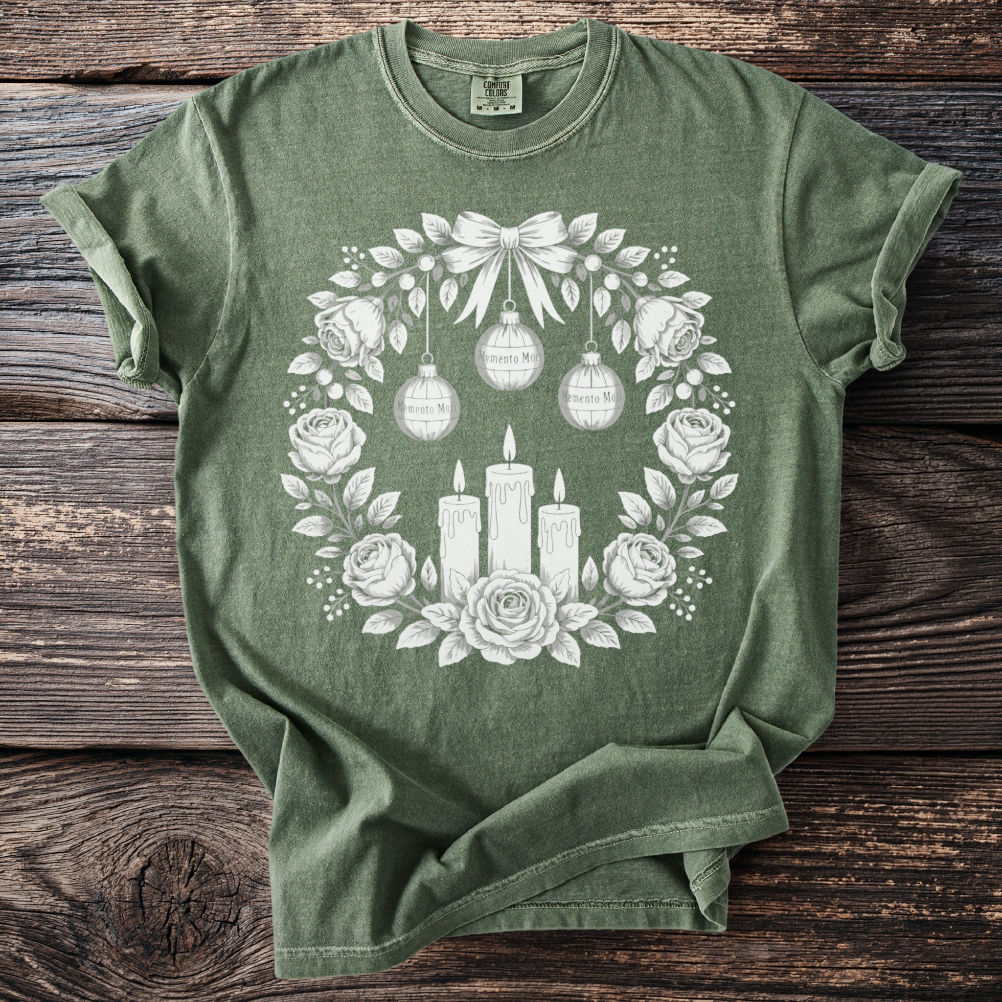 Green t-shirt with a white floral wreath, candles, and ornaments graphic.