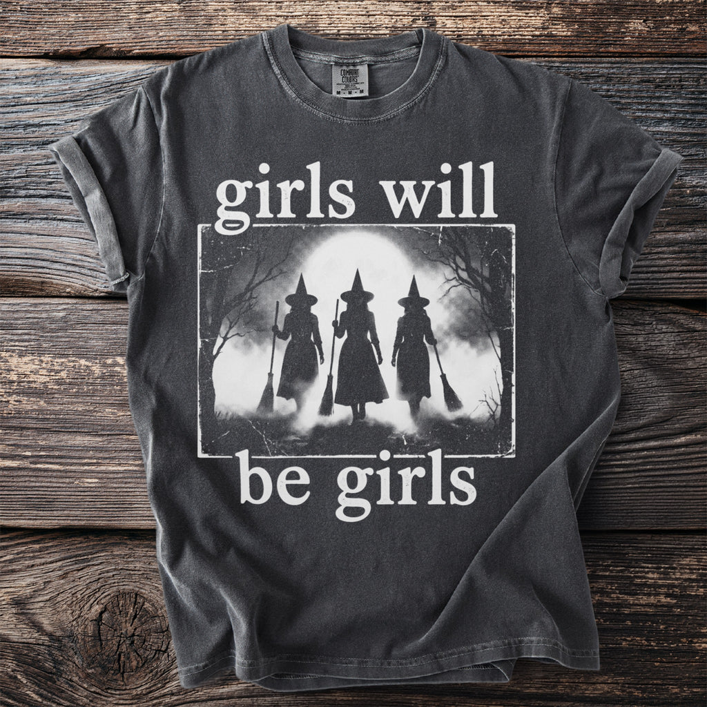Dark t-shirt with white text "girls will be girls" and silhouette of witches.
