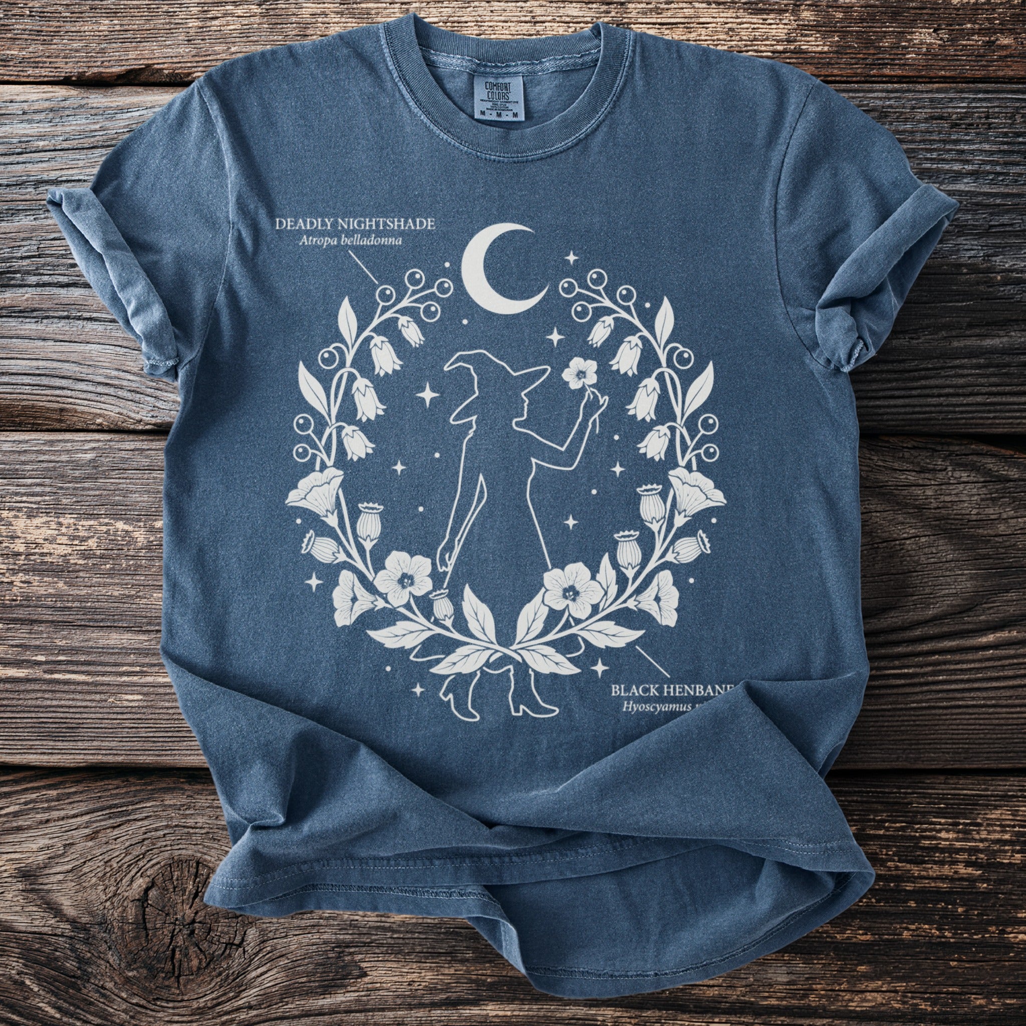 Blue t-shirt with white graphic of a witch, moon, stars, and medicinal plants.