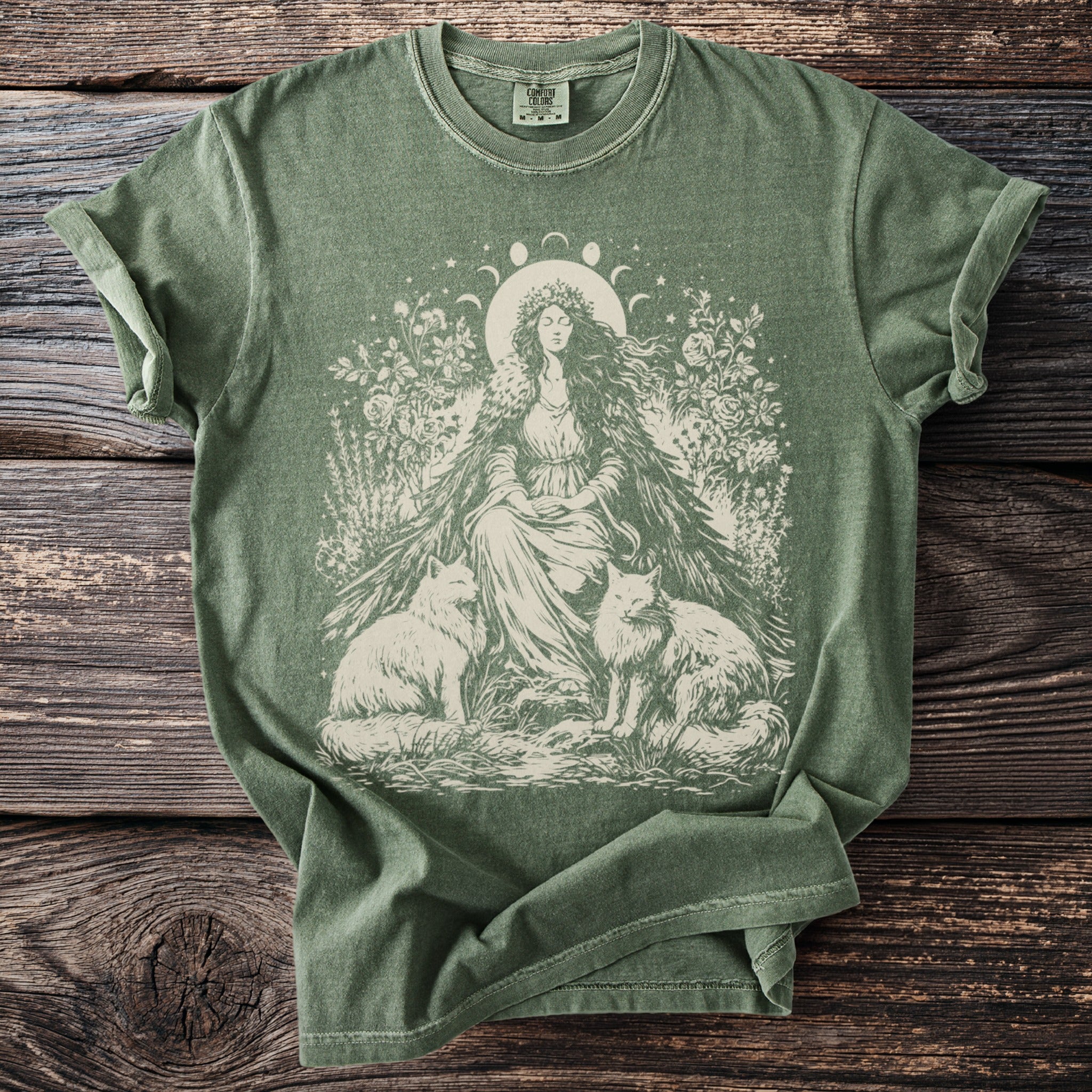 Olive green t-shirt with cream graphic of woman, two foxes, flowers, and moon phases.