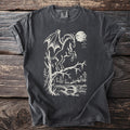 Dark grey t-shirt with a cream-colored winged creature on a tree branch.