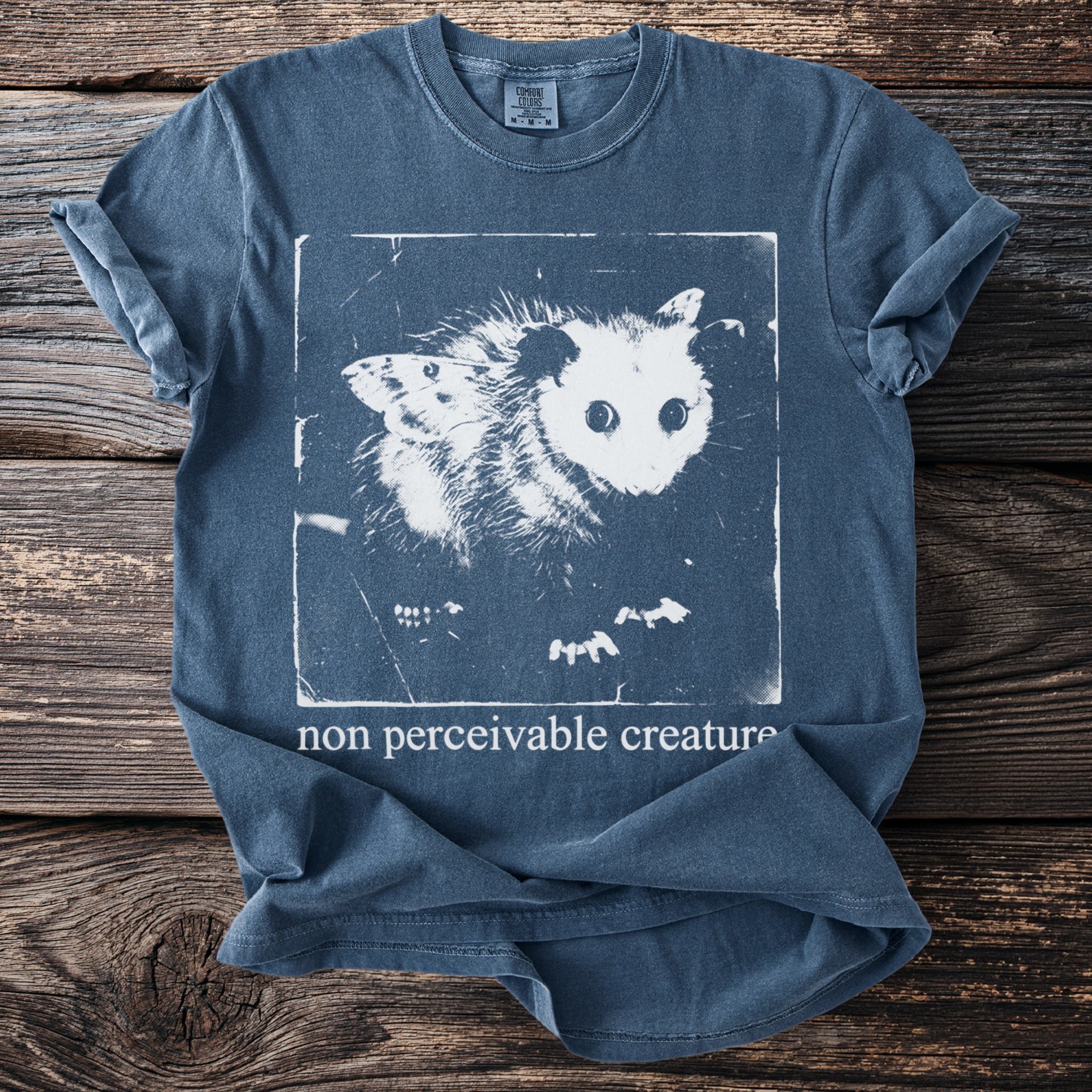 Blue t-shirt with a graphic of an opossum with butterfly wings and the text "non perceivable creature".