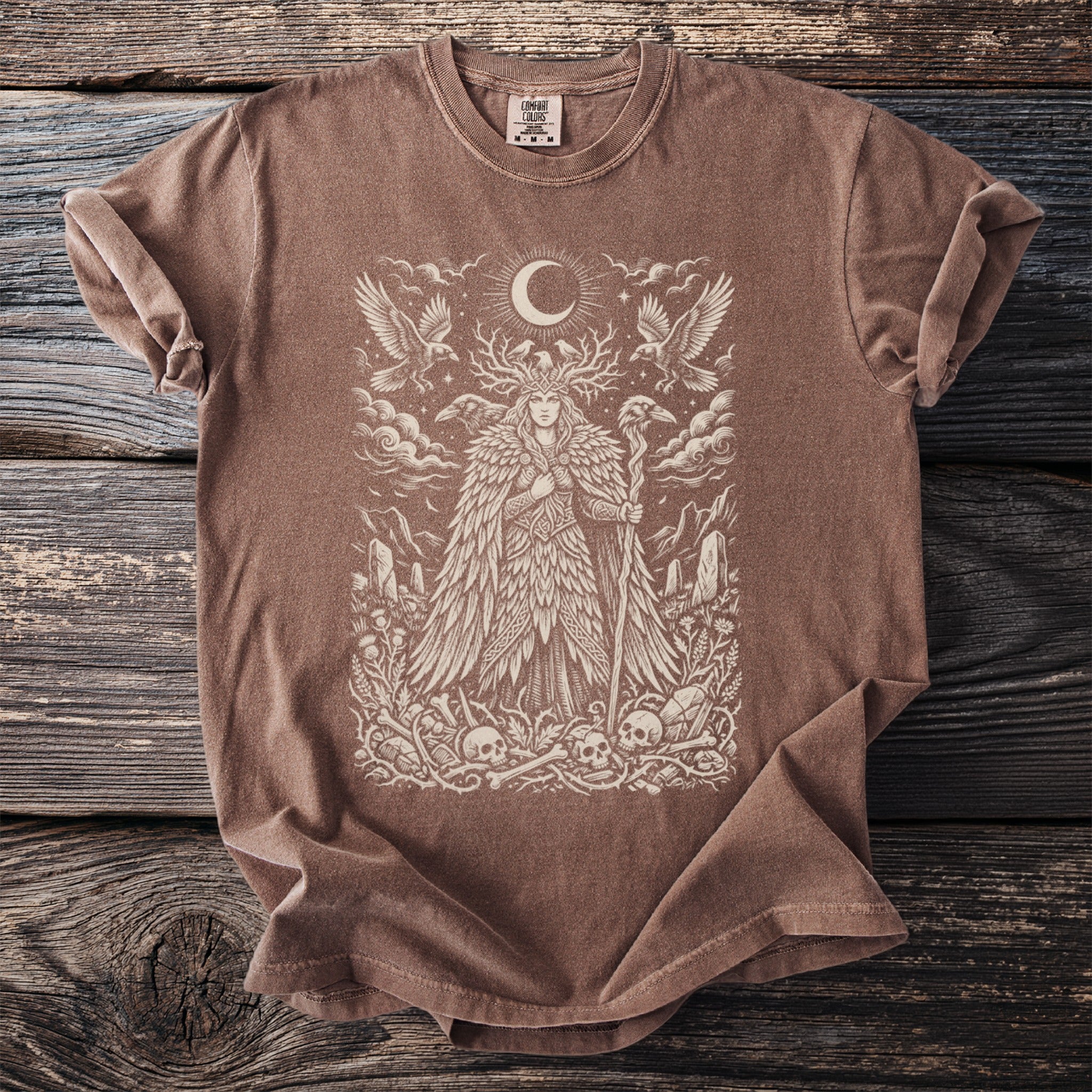 Brown t-shirt with a graphic of a woman with antlers, moon, birds, and skulls.