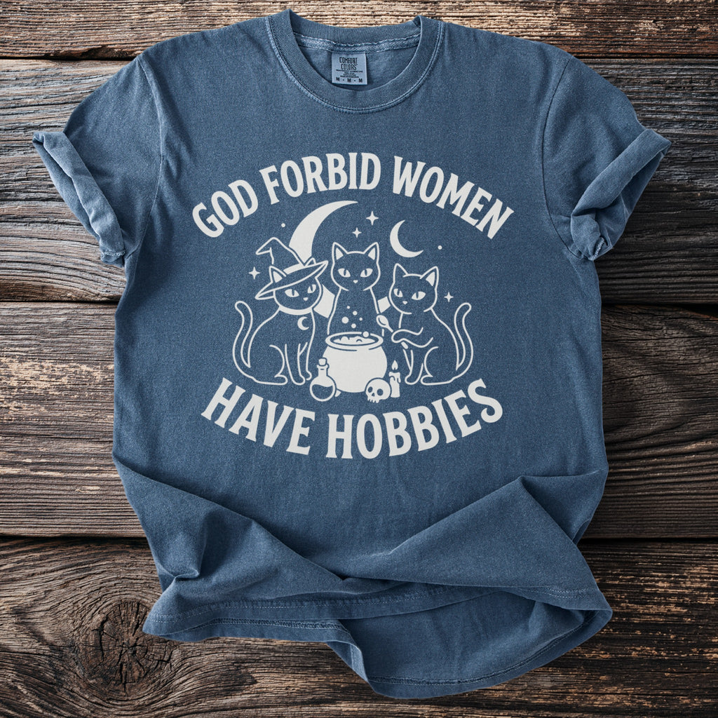 T-shirt with three cats gathered around a cauldron, reading "God Forbid Women Have Hobbies."