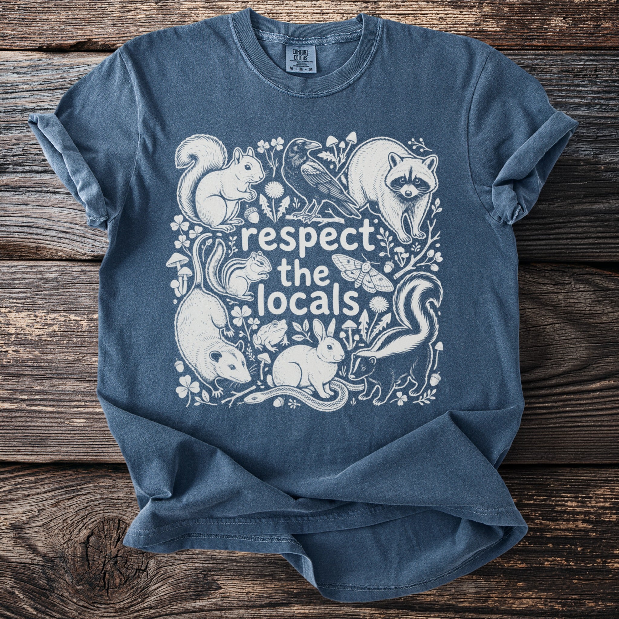 Blue t-shirt with white illustration of forest animals and text "respect the locals".