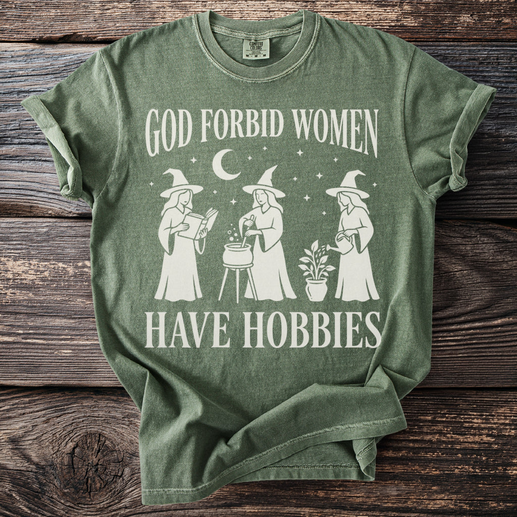 Green t-shirt with white text and illustrations of three witches and a plant.