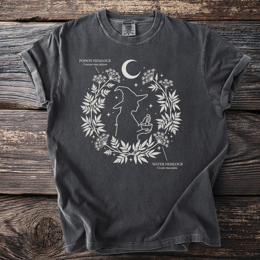 Dark grey t-shirt with white linework of a witch and medicinal plants, moon, and stars.