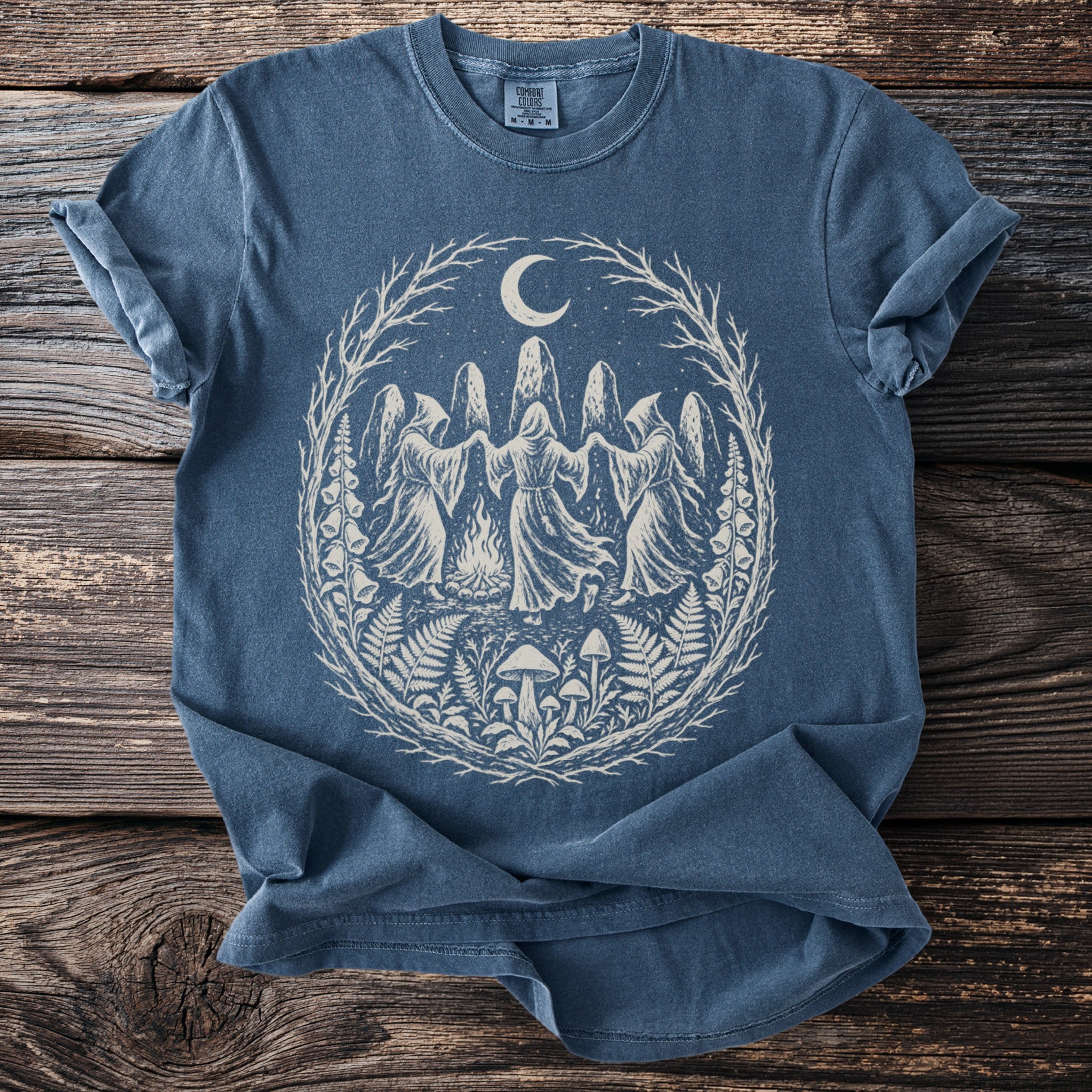 Blue t-shirt with a circular graphic of hooded figures dancing under a moon.