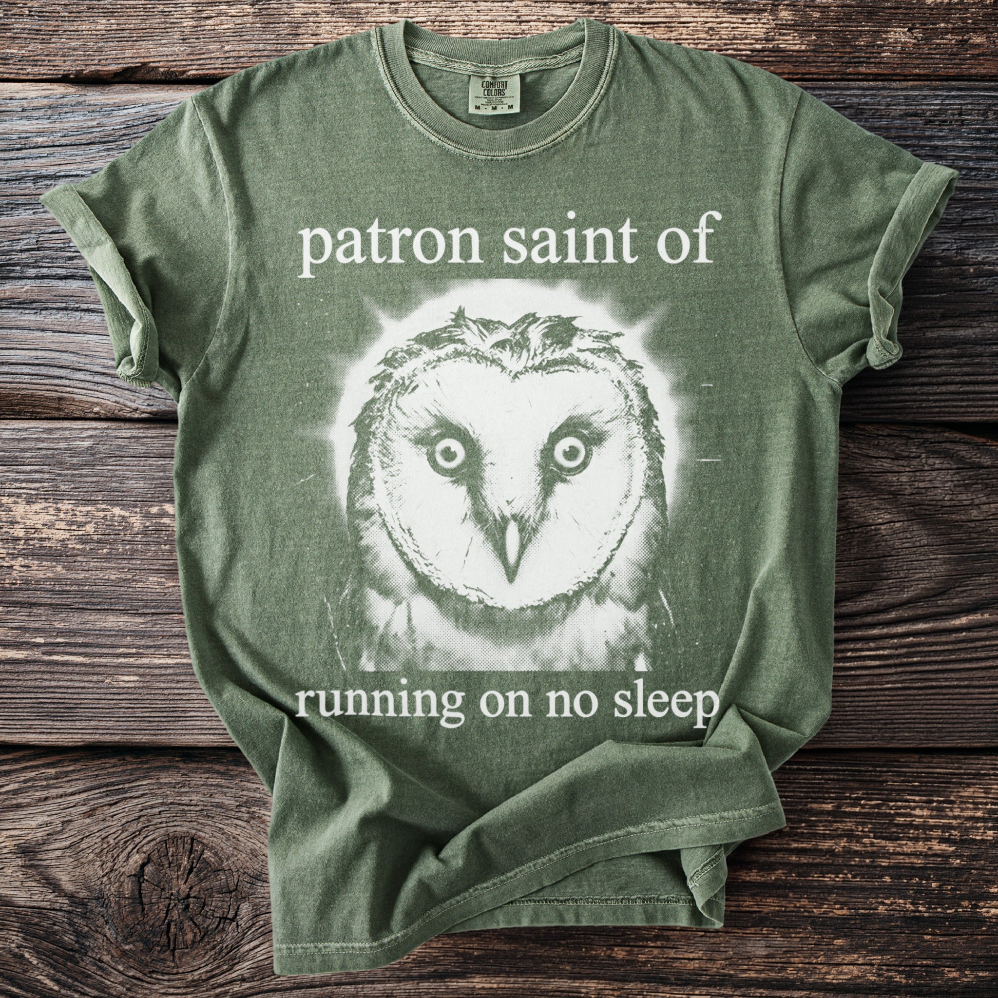 Olive green t-shirt with owl graphic and text "patron saint of running on no sleep".