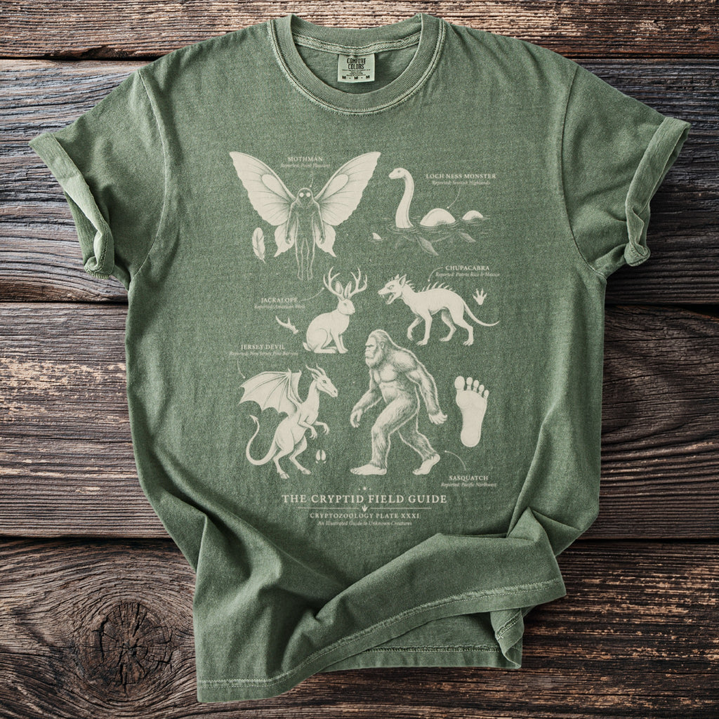 Green t-shirt featuring "The Cryptid Field Guide" with illustrations of Mothman, Loch Ness Monster, and Sasquatch.