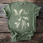 Green t-shirt featuring "The Cryptid Field Guide" with illustrations of Mothman, Loch Ness Monster, and Sasquatch.