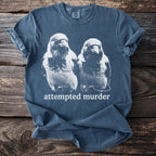 Blue t-shirt with a white distressed graphic of two birds and the text "attempted murder".
