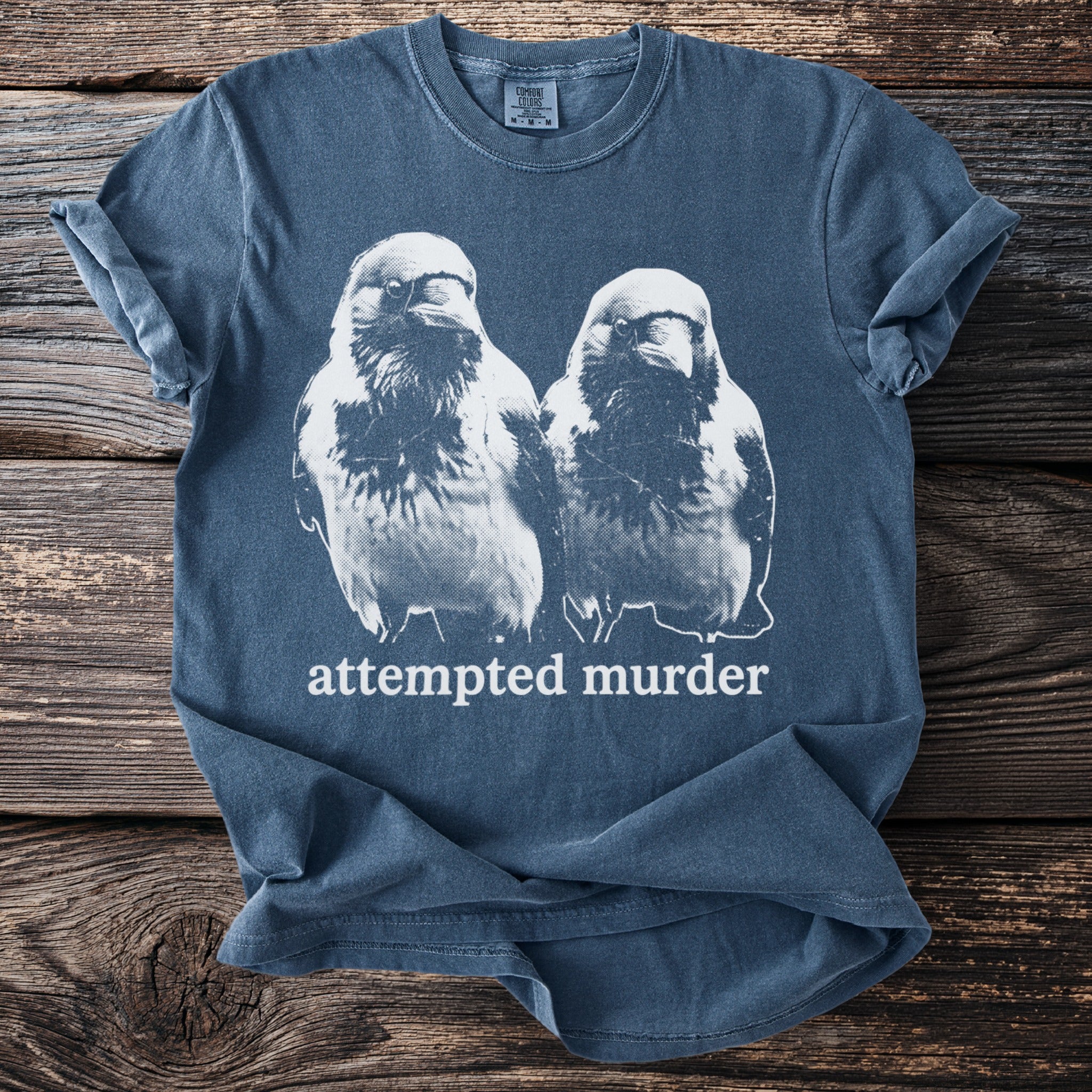 Blue t-shirt with a white distressed graphic of two birds and the text "attempted murder".