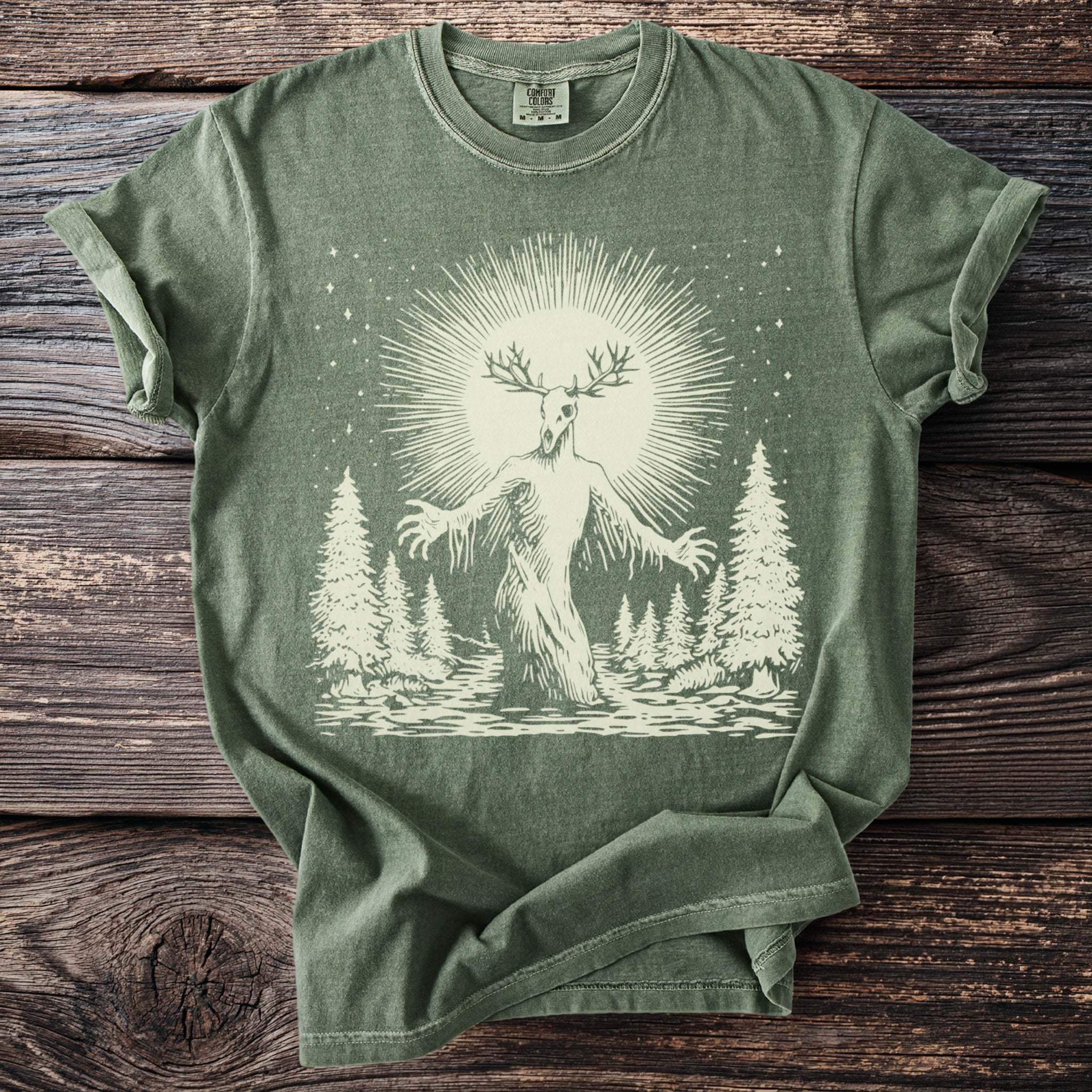 Green t-shirt featuring a creature with antlers in a forest scene with a sunburst.