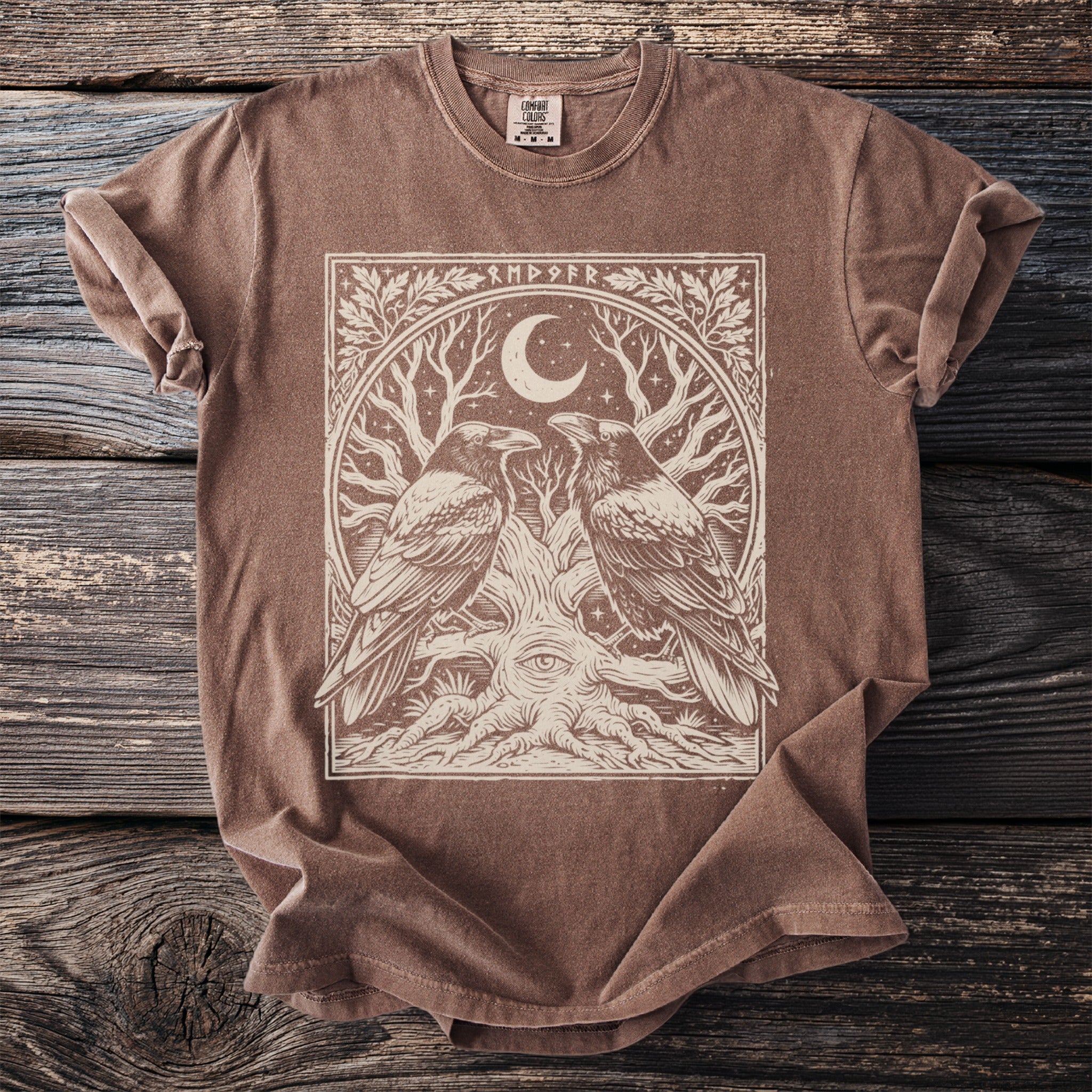 Brown t-shirt with a graphic of two ravens, a tree with an eye, moon, and runes.