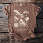 Brown t-shirt featuring a vintage illustration of cephalopods and ammonites titled "The Cephalopod Cabinet."