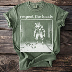 Green t-shirt with "respect the locals" text and wolf-man offering food to a cat.