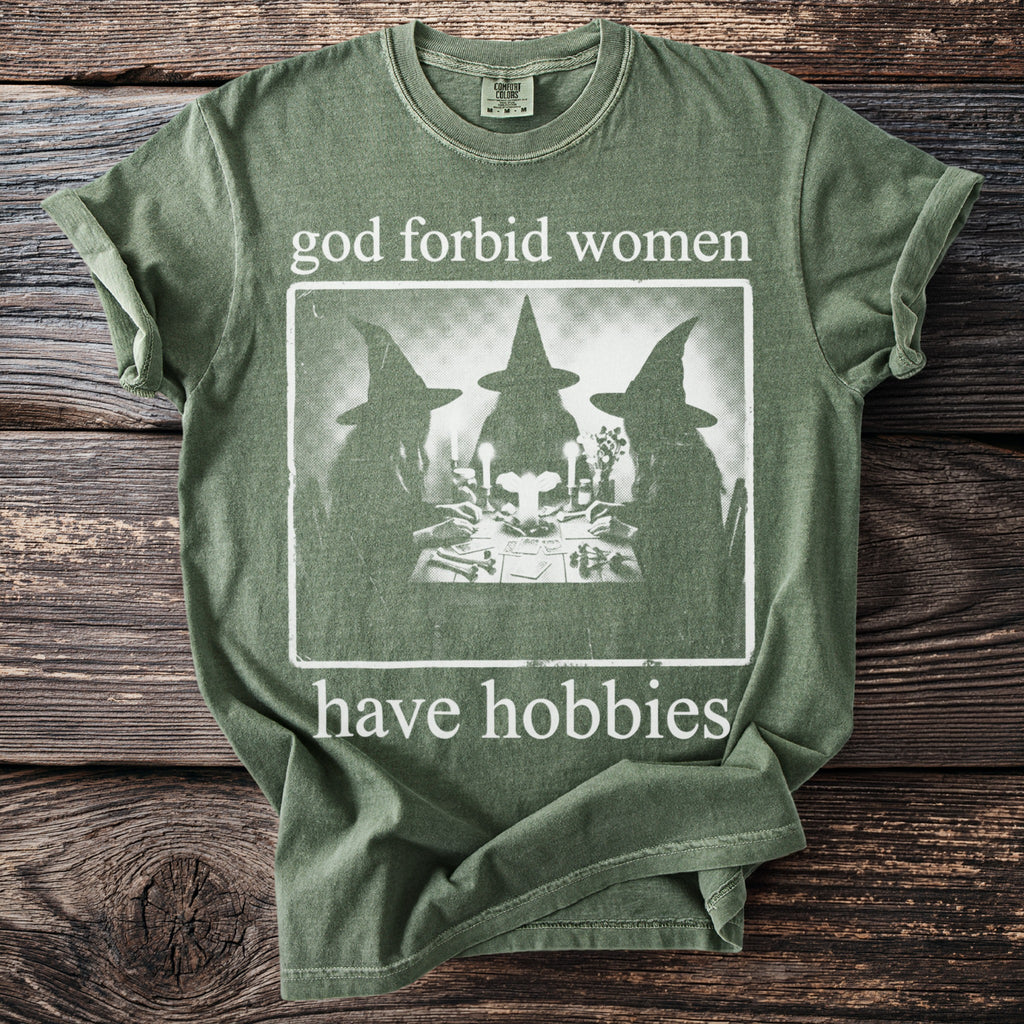 Green t-shirt with the text "god forbid women have hobbies" and a graphic of witches.