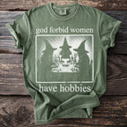 Green t-shirt with the text "god forbid women have hobbies" and a graphic of witches.