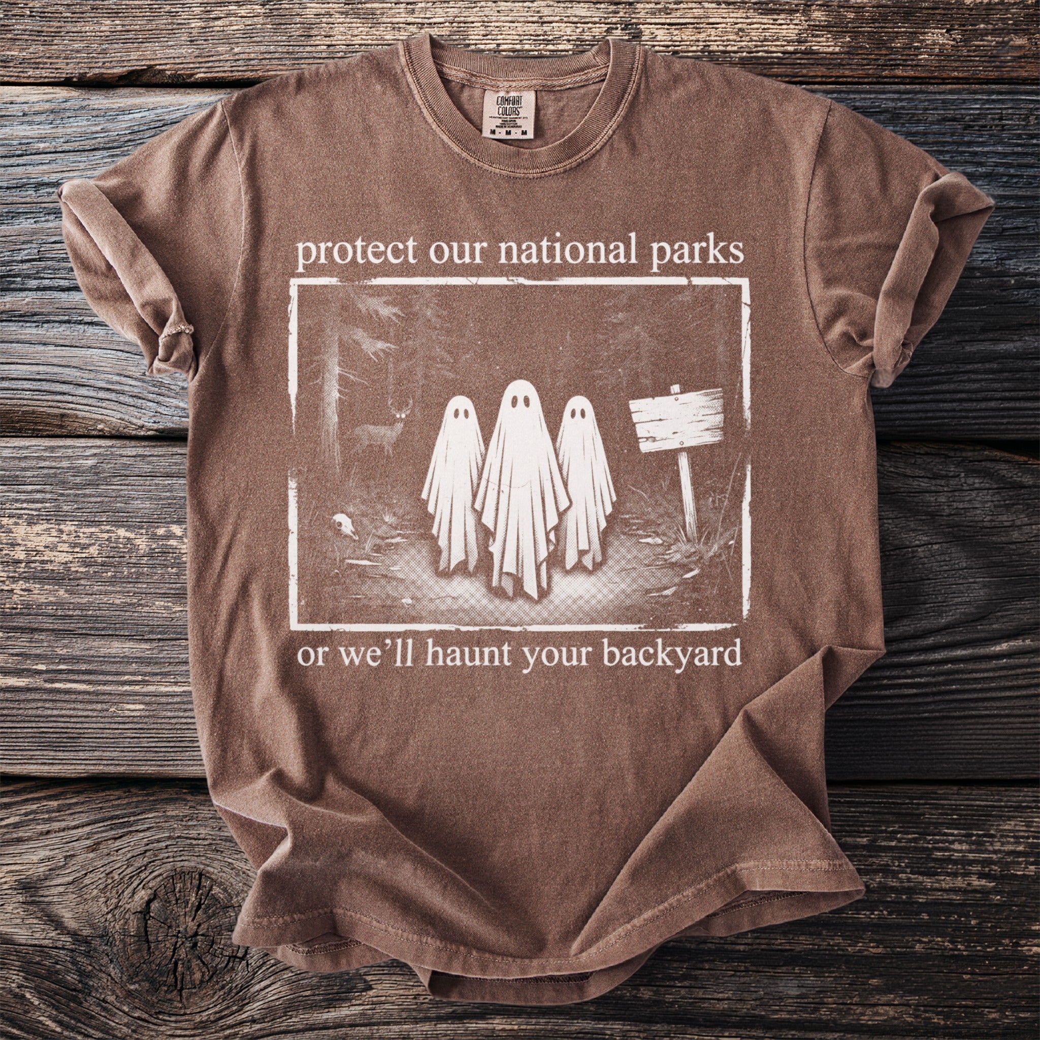 Brown t-shirt with "protect our national parks or we'll haunt your backyard" text and ghost graphic.