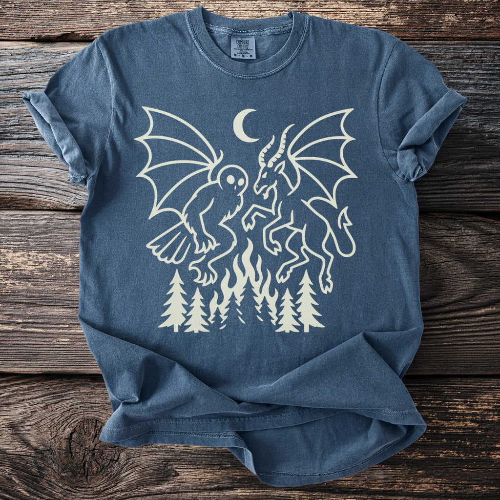Dark blue t-shirt with cream graphic of owl and demon battling over flames and trees.