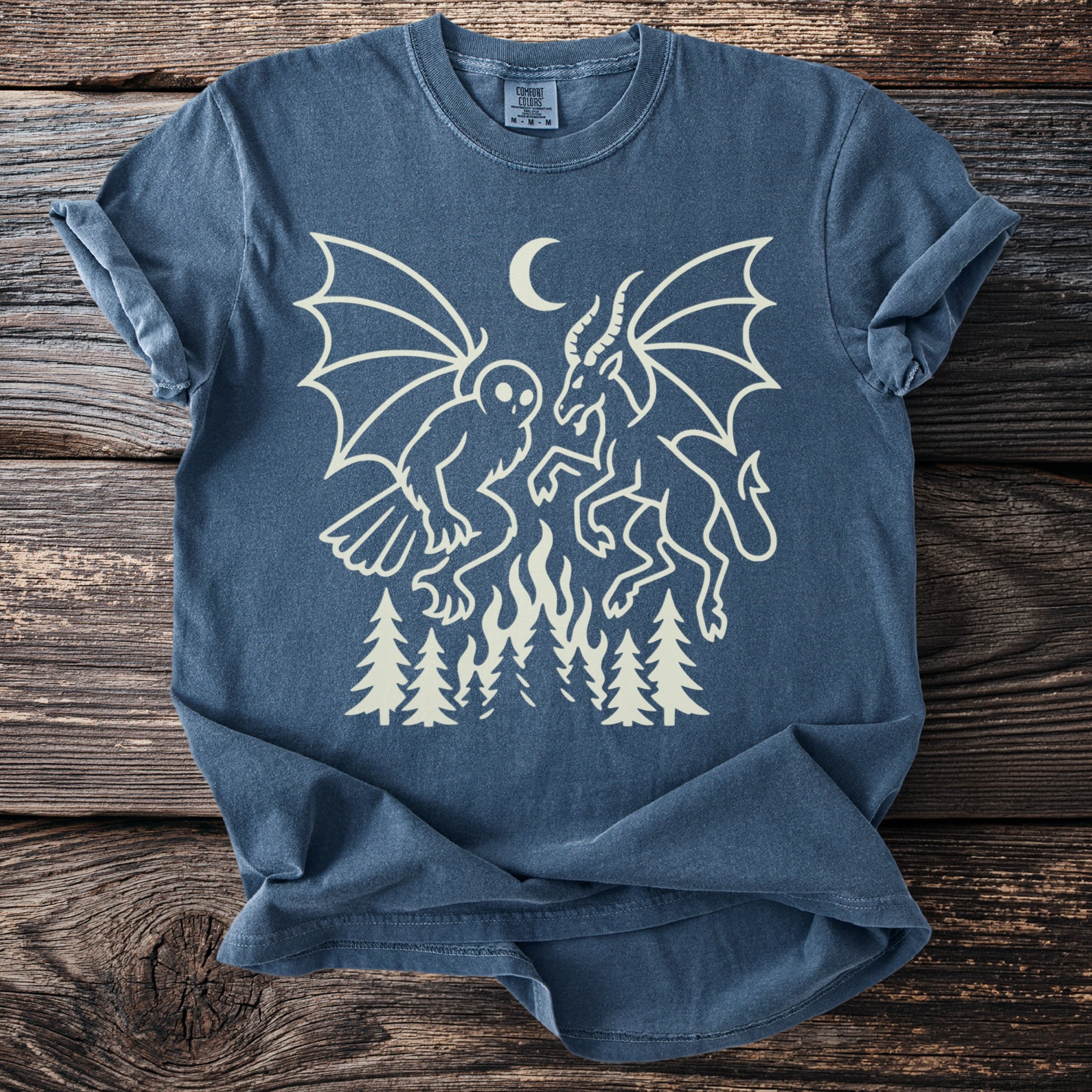 Dark blue t-shirt with cream graphic of owl and demon battling over flames and trees.