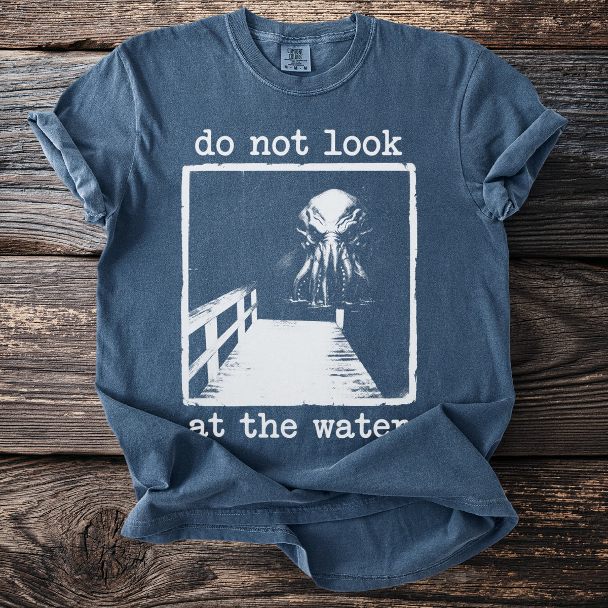 T-shirt with "do not look at the water" text and a tentacled creature on a dock.