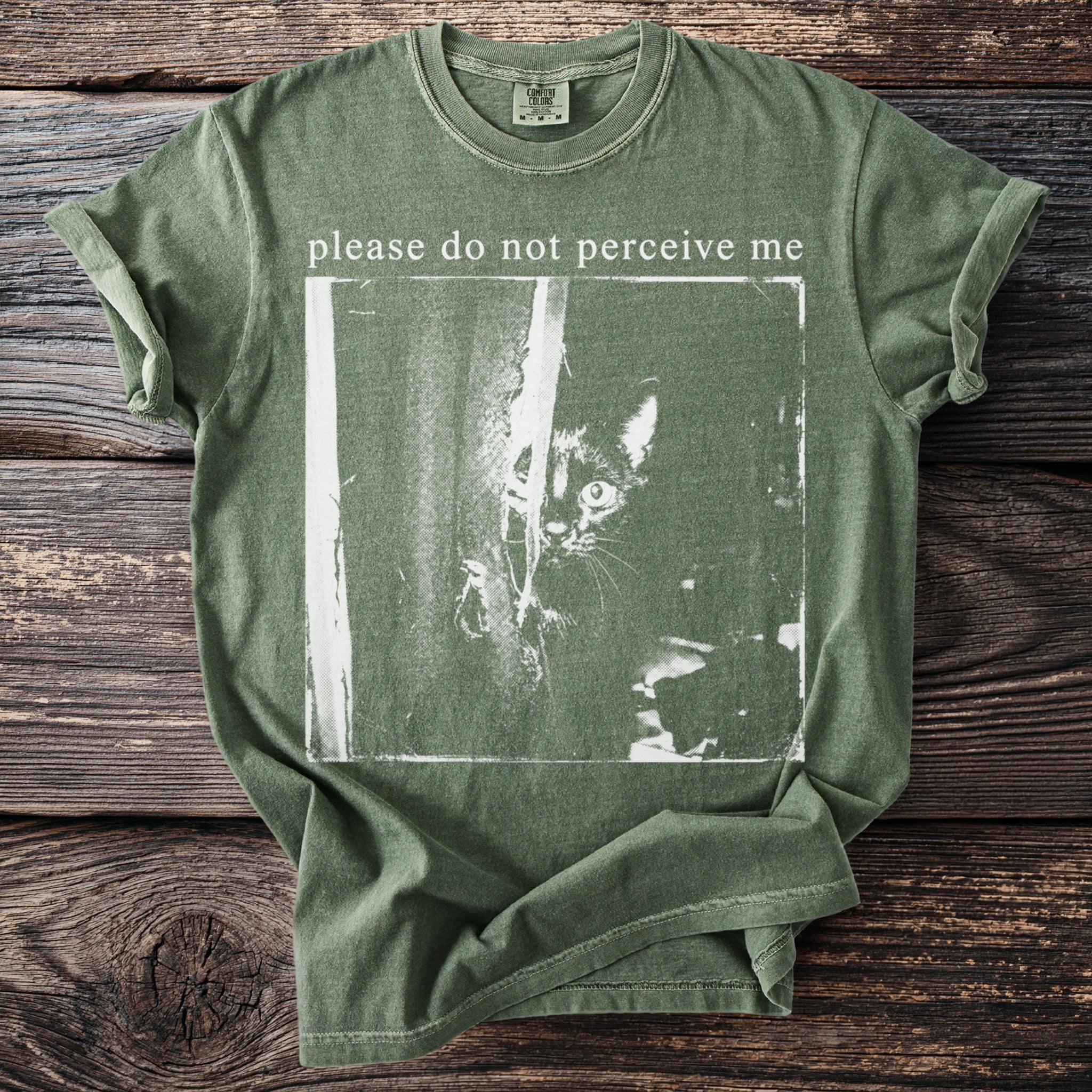Green t-shirt with white graphic of a black cat and text "please do not perceive me".
