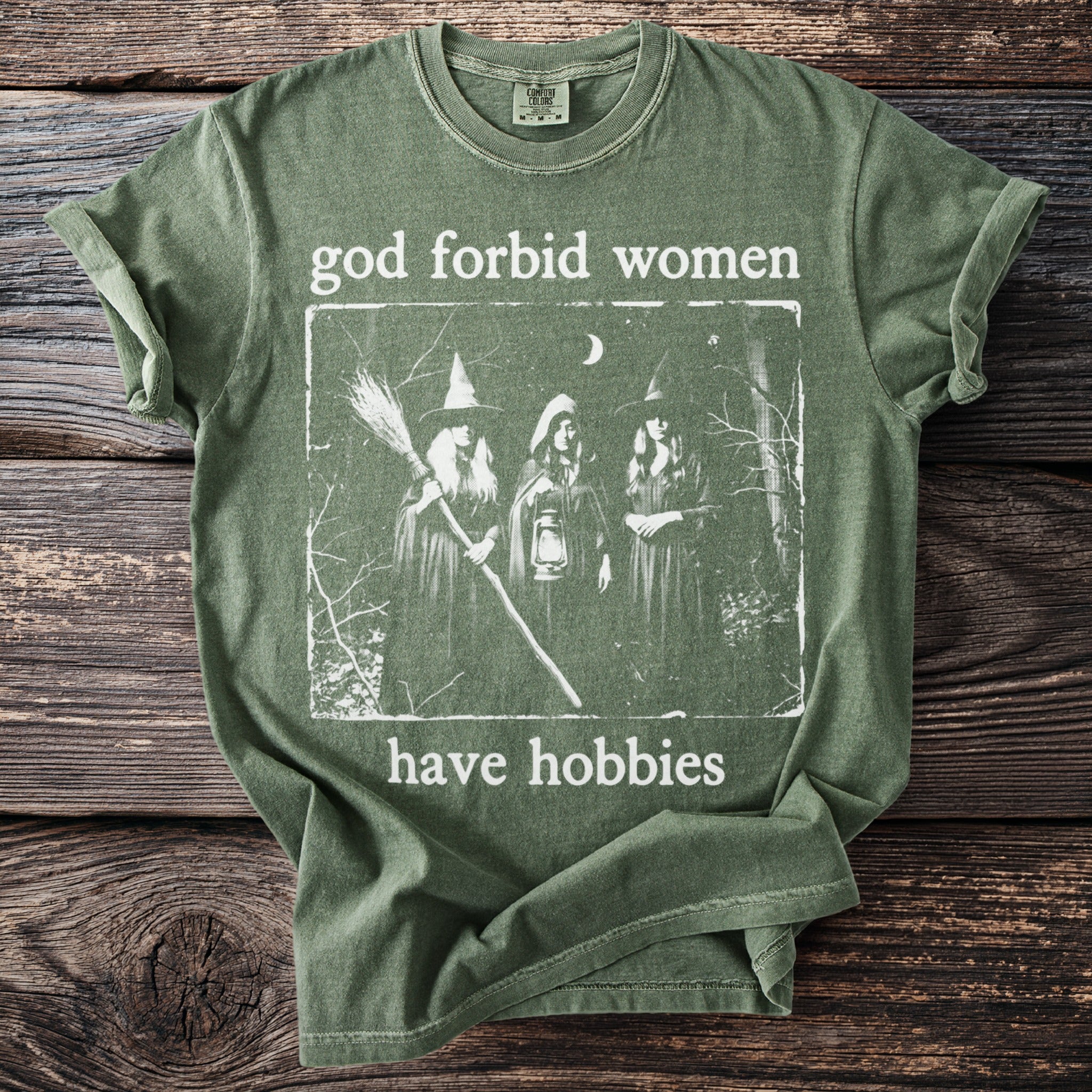 Green t-shirt with "god forbid women have hobbies" and three witches graphic.