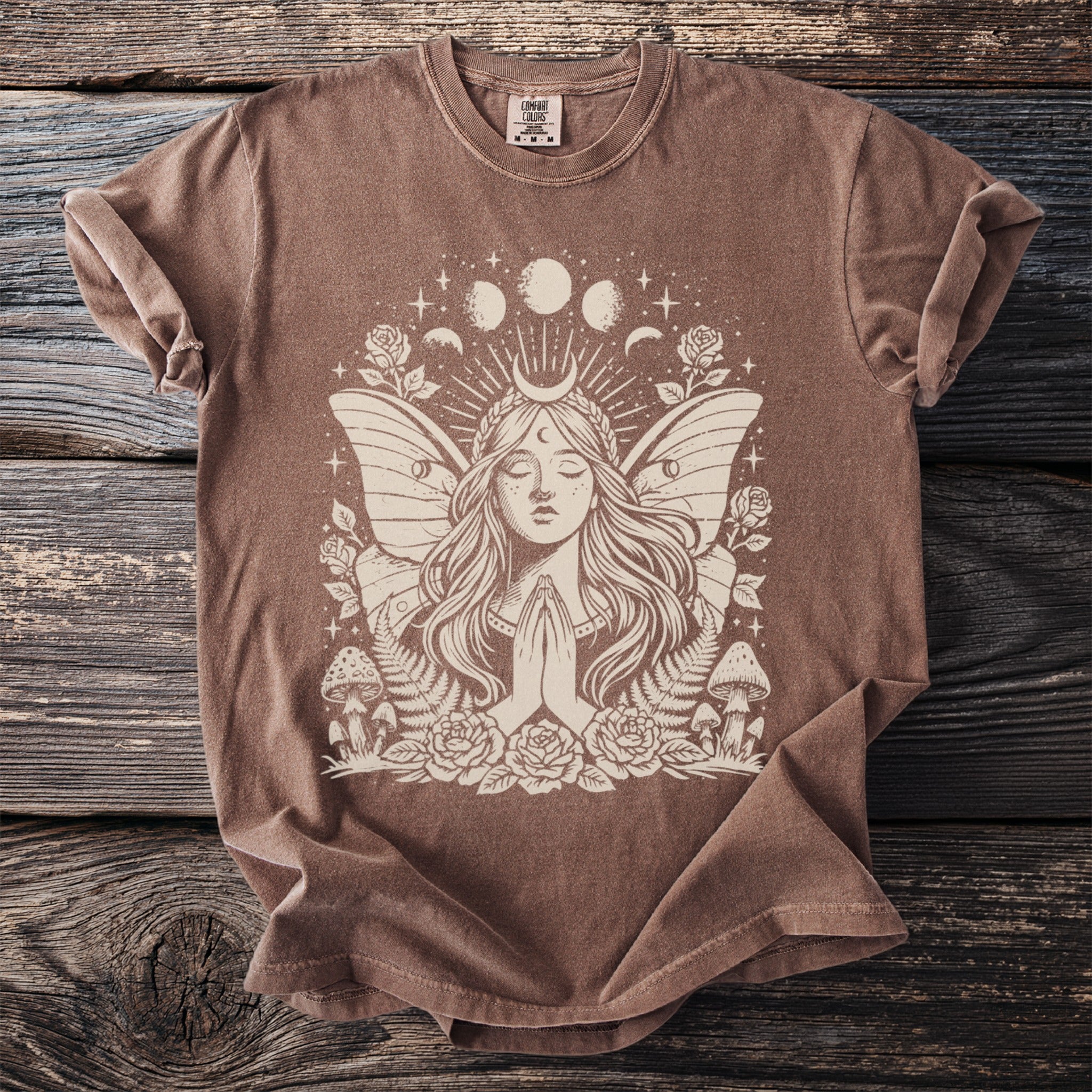 Brown t-shirt with a cream graphic of a winged fairy, crescent moon, and celestial elements.
