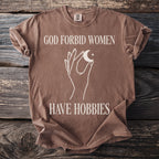 Brown t-shirt with white text "GOD FORBID WOMEN HAVE HOBBIES" and celestial graphic.