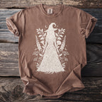 Brown t-shirt with a white line drawing of a witch figure wearing a floral dress.